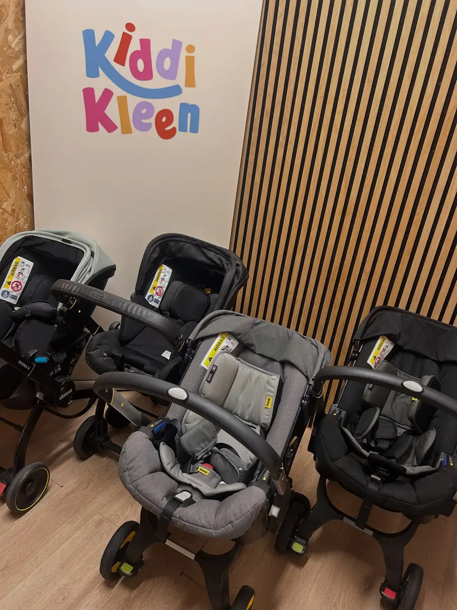 Four Doona car seats lined up in front of the Kiddi Kleen sign