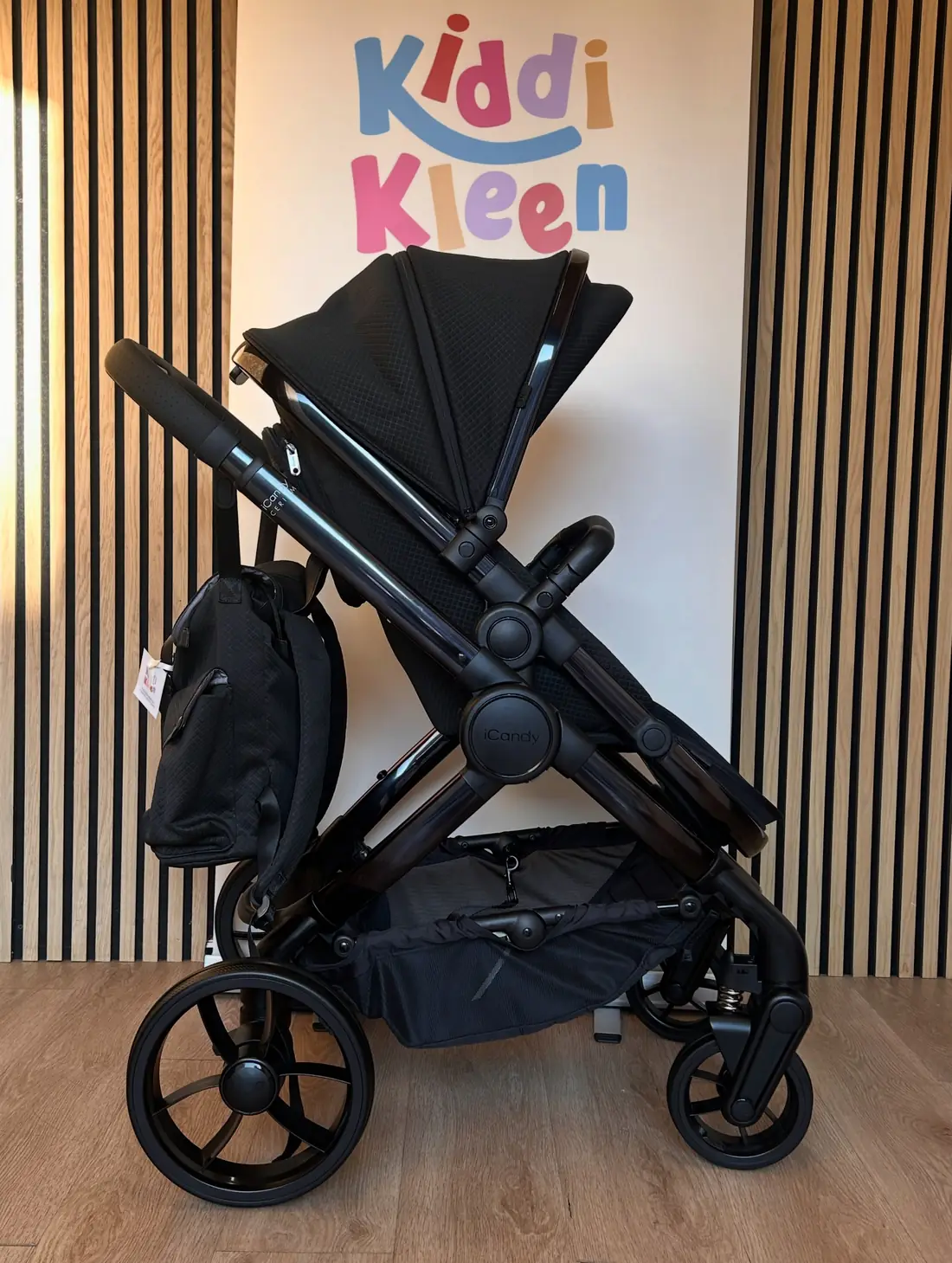 A freshly cleaned black iCandy pram in front of the Kiddi Kleen sign at the Johnstone workshop